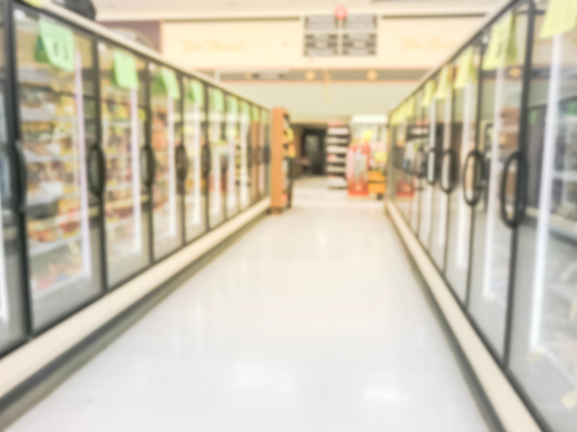 Blurred image frozen section at retail store in Texas, USA. Defocused huge glass door aisle with variety pack of processed fruit, vegetable, breakfast, appetizer, side, meals, pizza at grocery store